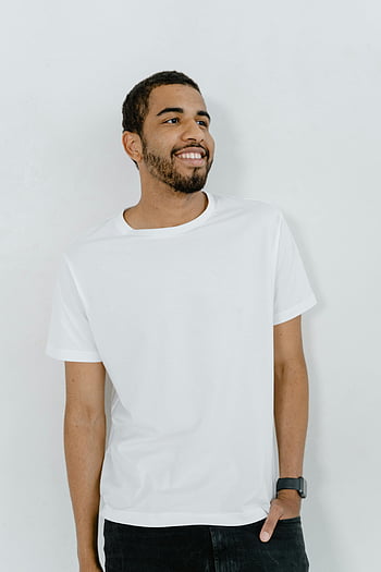 Mand i hvid t-shirt, hvid besætning hals t-shirt, Ung mand smiler, hænder i lommer, hvid baggrund, Casual outfit, mandlige mode, enkel baggrund, Hverdagsstil, afslappet look, Hvid T-shirt-stil
