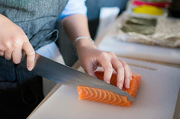 slicing meat, white chopping board, chef hands, fresh salmon, sushi preparation, cutting board, indoor cooking, salmon slicing, chef knife, food preparation, close-up shot