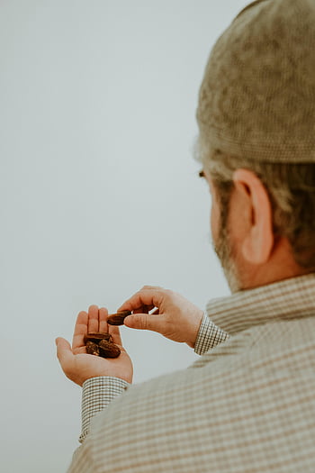 man holding dates, dates fruit, man wearing hat, plain background, back view, man with dates, holding dates, man in hat, dates in hand, man with beard, checkered shirt