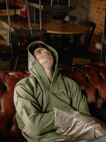 jonge man, groene hoodie, leren bank, gezellig huis, binnenomgeving, ontspannen pose, Vrijetijdsoutfit, woonkamer, comfortabele bank, huisdecoratie, lifestyle fotografie