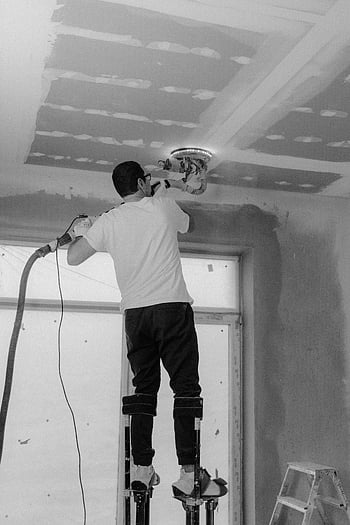 muž leštění stropu, Profesionální stropní lak, černobílá konstrukce, staveniště, renovace stropů, stropní práce, stavební dělník, stropní povrchování, Oprava stropu, Údržba stropu, Vnitřní konstrukce