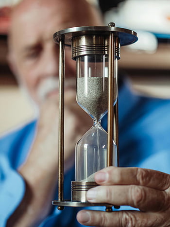 elderly man, metal hourglass, sand timer, clear hourglass, metal frame, holding hourglass, elderly person, sand flowing, time passing, close-up hourglass, aged hands