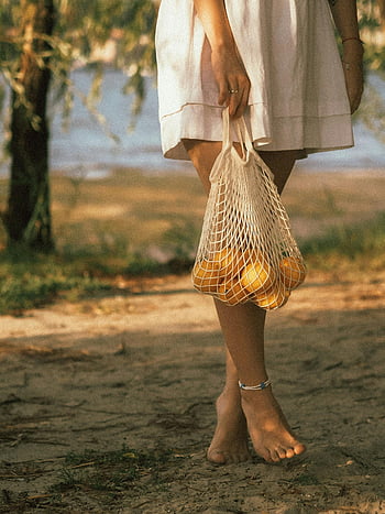 woman, white dress, mesh bag, lemons, barefoot, outdoors, yellow fruits, hand holding basket, natural setting, casual walk, anklet