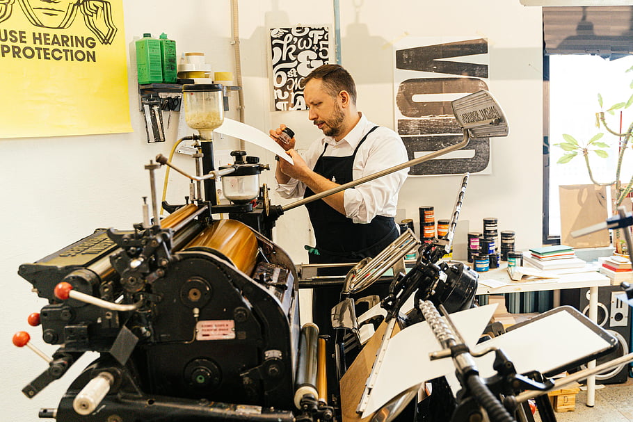 ember dolgozik, nyomtatóeszközök, Vintage Printing Press, műhelybeállítás, szaktudás, férfi kötényben, nyomdagépek, nyomtatási folyamat, műhely eszközök, nyomtatási műhely, vintage sajtó