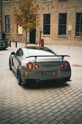 Gray Nissan GTR, back view, city street, brick buildings, sports car, parked, pavement, sleek design, urban setting, rear perspective, tail lights