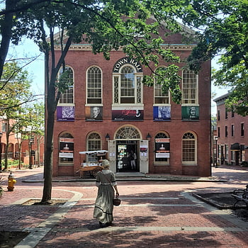 woman walking, brown brick town hall, historic charm, Boston brick architecture, landmark town hall, woman in dress, outdoor scene, historic building, town hall entrance, brick walkway, trees surrounding