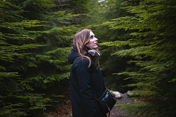 woman standing between trees, black coat, Tollymore Forest Park, Northern Ireland, lush greenery, forest exploration, outdoor adventure, nature walk, woman in forest, green trees, serene environment