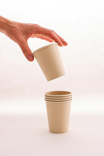stack of paper cups, biodegradable paper cups, hand stacking cups, neutral background, close-up photo, eco-friendly cups, disposable cups, paper cup stack, sustainable cups, cup stacking, white background