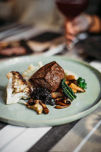 steak, grilled cauliflower, mushrooms, fine dining, restaurant setting, savory dish, plate presentation, gourmet meal, steak dinner, vegetable side, caviar garnish