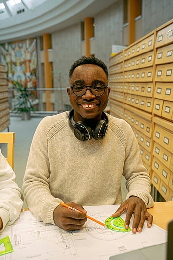 smiling man, working in library, architectural plans, university library, student studying, headphones, blueprint, educational setting, academic environment, library study, architectural design