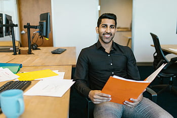 man in zwart shirt, Oranje map ingedrukt, lachende zakenman, modern kantoor, produktiviteit, bureau, documenten, kantooromgeving, professionele setting, werk ruimte, zakelijke kleding