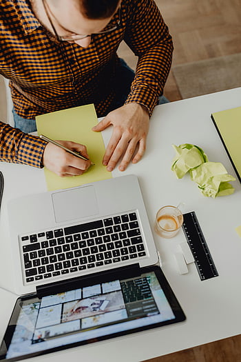 man skriver, högvinkelvy, Arbetar på bärbar dator, brevpapper på skrivbordet, skrivbord, bärbar dator och surfplatta, gul anteckningsblock, Skrynkligt papper, linjal, kaffekopp, rutig skjorta