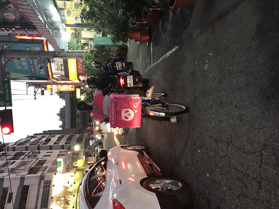 city street, motorcycle, delivery box, panda logo, car, traffic light, urban scene, night time, street signs, buildings, bicycles