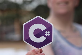 C# programming language, logo sticker, woman hand, outdoor photo, programming logo, C# sticker, person holding, outdoor setting, programming language logo, C# programming, hexagon logo