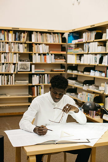 テーブルに座っている男、 建築家、 青写真、 ライブラリ設定、 計画プロジェクト、 精度、 焦点を絞った仕事、 本棚、 研究環境、 プロの仕事、 設計計画