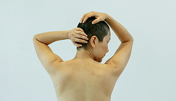 shirtless person, touching head, light background, studio portrait, thoughtful individual, from behind, displaying individuality, back view, natural pose, minimalistic setting, human expression