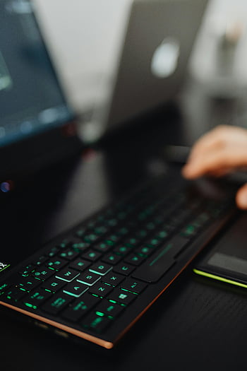 backlit keyboard, close-up shot, laptop keyboard, person using laptop, blurred background, computer keyboard, green backlight, workspace, technology, office setup, hands typing