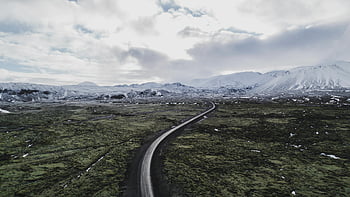 aerial view, winding road, Iceland, snow-capped mountains, open fields, winter, gray asphalt road, green grass field, white cloudy sky, landscape photography, aerial photography