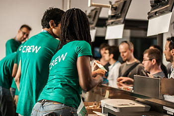 crew members, green shirts, event staff, customer service, counter interaction, people working, indoor setting, professional attire, team collaboration, service industry, customer engagement