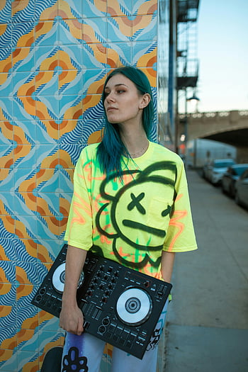 DJ, graffiti wall, urban setting, trendy young woman, neon t-shirt, music mixer, street art, vibrant colors, cityscape, modern fashion, DJ equipment