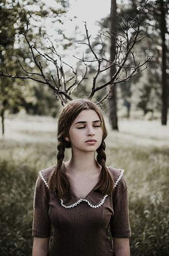 Teenager-Mädchen, braunes Kleid, geflochtenes Haar, Äste als Geweih, bezaubernde Waldszene, künstlerisches Porträt, Fotografie im Freien, von Natur aus inspiriert, junge Frau, Rustikaler Stil, Waldeinstellung