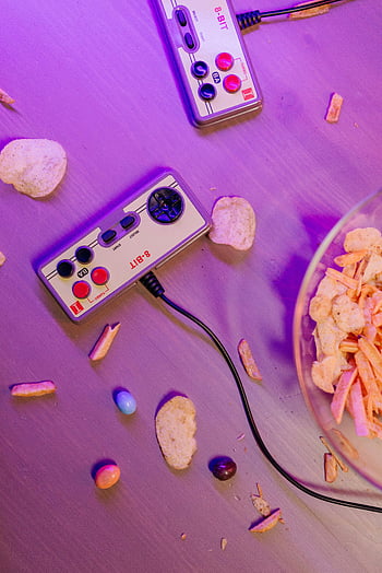 retro herní ovladače, roztroušené občerstvení, fialové osvětlení, stůl, 8bitové řadiče, bramborové hranolky, video hra, retro hry, občerstvení na stole, nastavení her, fialová atmosféra
