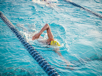 athlete swimming, yellow cap, front crawl, swimming pool, daytime swim, swimmer, pool lane, water sport, competitive swimming, outdoor pool, active lifestyle