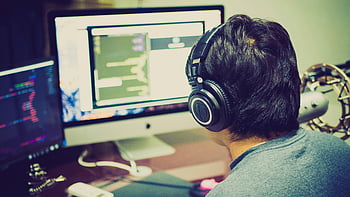 selective focus photography, man facing computer, programmer, headphones, coding, computer setup, dual monitors, software development, tech workspace, audio equipment, desk setup
