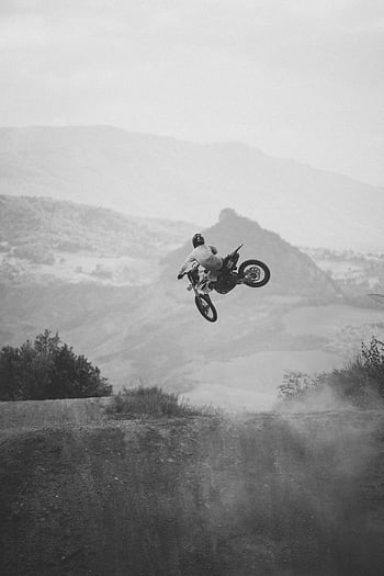 monochrome photo, motorcycle rider, motocross jump, scenic hills, Ravenna Italy, black and white, impressive jump, outdoor action, adventure sports, motorbike stunt, landscape backdrop