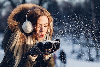 kvinde blæser sne, sne dag, Hyggelige øremuffer, vinter jakke, ung kvinde, nyder sne, vinter sjov, Udendørs vinteraktivitet, snefnug, vinter mode, vinter glæde