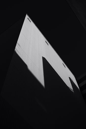 building, black background, low angle, black and white, geometric shadows, architectural patterns, monochrome, shadow play, modern architecture, minimalist, contrast