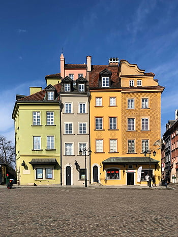 Warsaw Old Town, colorful buildings, cobblestone street, yellow concrete building, charming architecture, historic buildings, European cityscape, people walking, urban scene, sunny day, blue sky