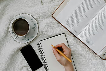 writing in notebook, open book, coffee in bed, cozy setup, reading, studying, handwriting, notebook, coffee cup, smartphone, bed setup