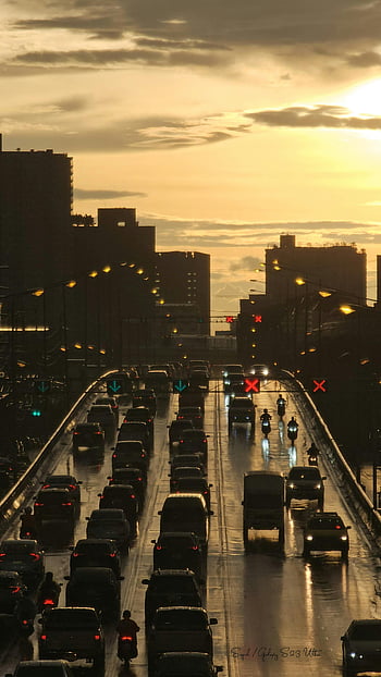 sunset traffic, bridge, Nonthaburi Thailand, rainy expressway, silhouetted skyline, cityscape, evening commute, urban scene, wet road, traffic lights, motorbikes