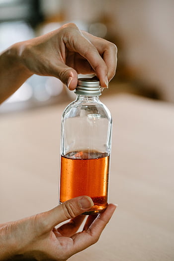hands holding bottle, orange liquid, glass bottle, beauty themes, health themes, close-up hands, liquid bottle, orange drink, beauty product, health product, natural liquid