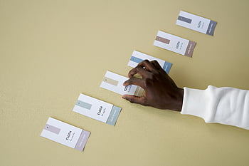 color swatch tags, yellow surface, person arranging, cloth labels, smooth surface, design elements, product display, tag arrangement, minimalist design, color samples, hand placement
