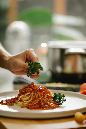 spaghetti bolognese, parsley garnish, homemade Italian cuisine, restaurant dish, close-up food photo, person adding greens, Italian pasta, food preparation, culinary art, spaghetti sauce, fresh herbs