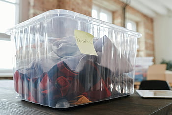donazione di vestiti, chiaro contenitore di plastica, scatola di donazione, donazione di abbigliamento, tavolo di legno, impostazione interna, donazione taggata, scatola di plastica, articoli di donazione, donazione organizzata, allestimento per donazioni al chiuso