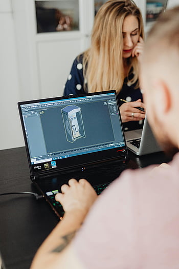 man using laptop, colleagues working, laptops indoors, 3D modeling software, indoor workspace, professional collaboration, technology use, focused work, office environment, digital design, teamwork