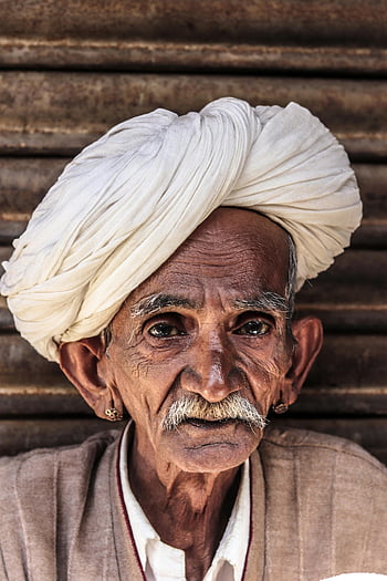 elderly man, white turban, brown shirt, close-up portrait, traditional turban, cultural heritage, mustache, earrings, wooden background, aged man, rich culture