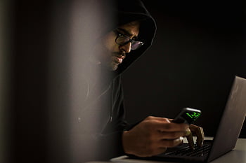 hacker etnico, smartphone, digitando, il computer portatile, buio, uomo in felpa con cappuccio, stanza buia, focalizzata, concentrato