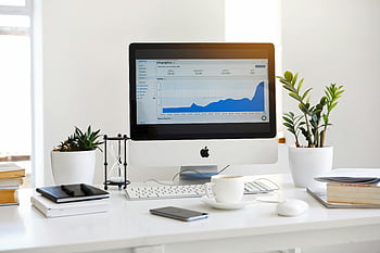 Silver iMac, line graph, desk workspace, contemporary workspace, analytics screen, plants, fresh look, white desk, office setup, modern office, workspace design