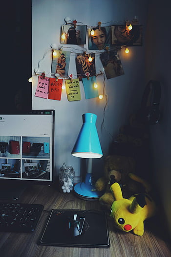 brown desk, assorted-color items, string lights, photos, blue lamp, warm desk setup, inviting desk, desk decor, plush toy, teddy bear, Pikachu plush