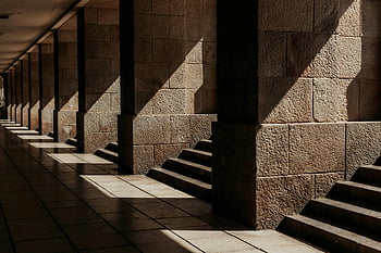 dramatic shadow play, stone corridor, sunlight patterns, stone columns, architectural corridor, steps, shadow, sunlight, stone architecture, architectural scene, dramatic lighting