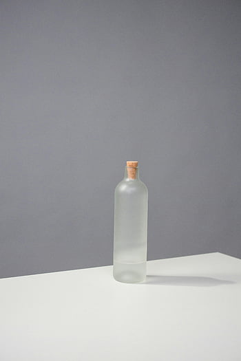 clear glass bottle, white table, gray background, studio photography, cork stopper, minimalist composition, white surface, transparent bottle, modern design, product photography, still life