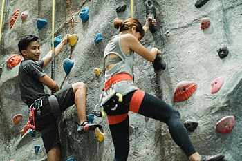 indoor rock climbing, safety harness, ethnic climbers, gym climbing, physical strength, focused duo, determined climbers, indoor climbing wall, young climbers, climbing gym, safety equipment