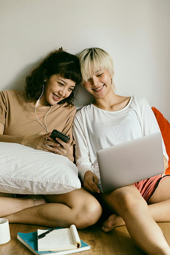 cheerful women, using smartphone, using laptop, smiling women, friendship, joy indoors, young women, devices, indoor setting, casual setting, technology use