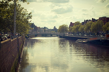 Gray Concrete Bridge, Tranquil city canal, historic bridge, tree-lined streets, cloudy sky, urban landscape, waterway scene, cityscape photography, peaceful urban view, bridge architecture, canal reflection