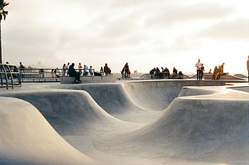 skateboard aréna, Venkovní skatepark, slunečný den, živá komunita, skateboardistů, diváků, skateboarding, Komunitní atmosféra, Betonové rampy, palmy, městské krajiny