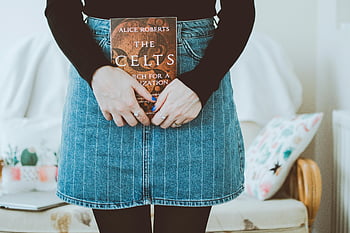 woman holding book, The Celts, cozy indoor setting, Alice Roberts, two hands, denim skirt, cozy room, indoor photo, book cover, casual outfit, home setting